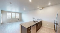 Located at 7128 NW 159th Ave in Portland, Oregon, this one-bedroom, one-bathroom unit offers a well-designed single-level layout that maximizes every square foot. The open-concept kitchen and living area serves as the heart of the home, featuring a granite-topped peninsula with an integrated sink, dark espresso cabinetry with brushed nickel hardware, and a full suite of stainless steel appliances including a refrigerator, range, and microwave. Light wood-style flooring runs throughout the main living areas, contributing to a clean, modern aesthetic. The living room receives ample natural light through a bank of windows that frame neighborhood views, creating a bright and welcoming atmosphere. A private entry door with a sidelight window adds convenience and additional natural light to the space. The bedroom is carpeted for comfort and includes a spacious sliding double-door closet, with windows that continue the theme of natural light. The bathroom is finished with matching granite countertops, dark cabinetry, and wood-style tile flooring, maintaining a consistent design language throughout. Neutral warm-toned walls and clean white trim unify the space, giving it a move-in-ready feel well-suited for comfortable everyday living.