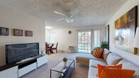 This single-floor residence offers a thoughtfully designed layout that balances comfort and functionality throughout its living spaces. The open-concept living and dining area is bright and welcoming, featuring plush carpeting, a ceiling fan with light fixture, and a textured ceiling. A sliding glass door floods the living room with natural light and provides access to an outdoor balcony, offering pleasant views of the surrounding greenery. The living room comfortably accommodates a sectional sofa, glass coffee table, and entertainment center, while the adjacent dining area provides space for a table and chairs beneath a window. The kitchen is efficiently laid out with warm honey-toned cabinetry, dark granite-style countertops, and durable tile flooring. It is fully equipped with white appliances including a refrigerator, dishwasher, electric range, and over-the-range microwave, along with ample upper and lower cabinet storage. The bedroom is a serene retreat with soft carpeting, a ceiling fan, and a mirrored sliding closet door that enhances the sense of space. The bathroom features a double-sink vanity with matching cabinetry, dark countertops, tile flooring, and a tiled shower-tub combination, providing a clean and functional design throughout.