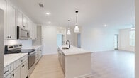 Located at 100 Wilton Cir S in Palm Coast, Florida, this well-appointed single-story home offers three bedrooms, two bathrooms, and a thoughtfully designed open-concept floor plan. The kitchen serves as a central showpiece, featuring a large white quartz island with a matte black faucet and sink, sleek gray shaker-style cabinetry, a classic subway tile backsplash, stainless steel appliances, and stylish pendant lighting — all flowing seamlessly into the dining and living areas. Light wood-look flooring runs throughout the main living spaces, creating a bright and cohesive feel, while large windows and sliding glass doors invite abundant natural light. The bedrooms are finished with plush carpeting and ceiling fans, each offering comfortable proportions. The primary bedroom includes access to generous closet space. The bathrooms are outfitted with white quartz vanities, matte black hardware, and a glass-enclosed walk-in shower with subway tile surround. A dedicated laundry room and an impressive seven closets provide exceptional storage throughout the home. The overall aesthetic is clean, modern, and move-in ready, reflecting a fresh and contemporary design sensibility well-suited to Florida living.