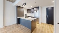 This contemporary 43 square meter apartment in Montréal offers a harmonious blend of modern design and functionality. The space is characterized by its open-concept layout, maximizing the use of the single-floor plan. The main living area features warm hardwood flooring and an exposed concrete ceiling, creating an industrial-chic ambiance.

The kitchen is a standout feature, boasting sleek grey cabinetry, stainless steel appliances, and a substantial island with a white countertop and integrated sink. Track lighting and pendant fixtures provide both task and ambient illumination.

The bedroom, while compact at 8 square meters, benefits from a large window that floods the space with natural light. Built-in storage solutions help maximize the available space.

The bathroom showcases a modern aesthetic with a floating vanity, large mirror, and built-in storage. Grey tile flooring complements the overall color scheme, while the white fixtures maintain a clean, fresh look.

Throughout the apartment, large windows offer views of the urban surroundings and allow ample daylight to penetrate the space. The efficient layout ensures that every square meter is utilized effectively, making this apartment an ideal urban dwelling for those seeking a contemporary lifestyle in the heart of Montréal.