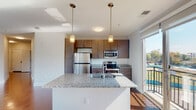 Located at 601 Jackson St in Durham, NC, this modern single-floor residence offers a thoughtfully designed open-concept layout that seamlessly connects the kitchen, dining, and living areas. Rich hardwood flooring runs throughout the main living spaces, reflecting natural light that pours in through large windows and a full-height sliding glass door leading to a private balcony with open outdoor views.

The kitchen is a standout feature, centered around a generous granite-topped island with a double sink and pendant lighting overhead. Dark wood cabinetry provides ample storage, while a full suite of stainless steel appliances — including a refrigerator, electric range, and built-in microwave — completes the space with a polished, contemporary feel.

The living area is bright and spacious, equipped with a ceiling fan and multiple windows that invite natural light from multiple angles. Bedrooms are finished with plush carpeting, ceiling fans, and windows offering views of the surrounding greenery, creating a calm and comfortable retreat.

Bathrooms feature clean white tiled tub-shower combinations with built-in shelving and brushed nickel fixtures, maintaining a crisp, functional aesthetic throughout. The overall design balances modern finishes with a welcoming, livable atmosphere well-suited to everyday comfort.