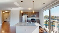 Located at 601 Jackson St in Durham, NC, this modern single-floor residence offers a thoughtfully designed open-concept layout that seamlessly connects the kitchen, dining, and living areas. Rich hardwood flooring runs throughout the main living spaces, reflecting natural light that pours in through large windows and a full-height sliding glass door leading to a private balcony with open outdoor views.

The kitchen is a standout feature, centered around a generous granite-topped island with a double sink and pendant lighting overhead. Dark wood cabinetry provides ample storage, while a full suite of stainless steel appliances — including a refrigerator, electric range, and built-in microwave — completes the space with a polished, contemporary feel.

The living area is bright and spacious, equipped with a ceiling fan and multiple windows that invite natural light from multiple angles. Bedrooms are finished with plush carpeting, ceiling fans, and windows offering views of the surrounding greenery, creating a calm and comfortable retreat.

Bathrooms feature clean white tiled tub-shower combinations with built-in shelving and brushed nickel fixtures, maintaining a crisp, functional aesthetic throughout. The overall design balances modern finishes with a welcoming, livable atmosphere well-suited to everyday comfort.