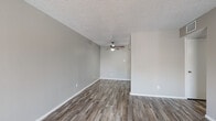 This single-floor unit offers a cohesive and functional layout with consistent wood-look flooring running throughout every room, tying the space together with a warm, neutral aesthetic. The living area is generously proportioned, featuring a ceiling fan with light fixture and a textured ceiling. A sliding glass door floods the space with natural light and provides access to an outdoor area, offering a view of the surrounding exterior. The open layout connects the living space to the galley-style kitchen, which is efficiently designed with white cabinetry, speckled gray countertops, a white electric range, a refrigerator, a dishwasher, and a tile backsplash. Upper and lower cabinets provide ample storage throughout. The bedroom is a comfortable, well-lit room with a ceiling fan, natural light from a window with blinds, and matching wood-look flooring. The full bathroom includes a combined tub and shower unit with white tile surround, a toilet, and overhead cabinetry for additional storage. Neutral gray wall tones and white trim are consistent throughout, contributing to a clean and modern appearance. The textured ceilings and practical finishes complete the overall character of this straightforward, move-in-ready space.