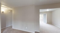 Located at 14222 Dallas Pkwy in Dallas, TX, this single-floor unit offers a practical and comfortable layout designed for everyday living. The open-concept kitchen features white cabinetry, dark countertops, a black refrigerator, and a peninsula that separates it from the adjacent living area. Wood-style flooring in the kitchen transitions to plush carpeting throughout the living and bedroom spaces, adding warmth underfoot. The living area is generously proportioned, bathed in natural light from a large window, and features neutral-toned walls with a textured ceiling. Multiple rooms include sliding glass doors and vertical blinds that provide outdoor views and access to balcony-style spaces, allowing natural light to filter throughout. The bedrooms are well-sized with soft carpeting, closet access, and a calm, neutral color palette. Two bathrooms are present, each equipped with a tiled shower-tub combination, dark countertop vanity, and wood-style flooring. The overall ambiance of the space is clean, functional, and move-in ready, with a consistent neutral color scheme that provides a versatile backdrop throughout.