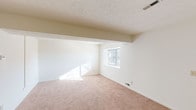 This two-floor residence offers a practical and well-organized layout across multiple rooms. The living areas are finished with warm beige carpet throughout, creating a cohesive look while textured ceilings add subtle dimension overhead. Structural beam details are visible in the main living space, which receives natural light through a window overlooking mature trees outside.

The kitchen is equipped with warm medium-tone wood cabinetry, light granite-style countertops, and white appliances including a refrigerator, electric range, and dishwasher. Wood-look flooring ties the kitchen together and provides easy maintenance underfoot.

The bedrooms are spacious and carpeted, each featuring built-in closet storage with shelving and hanging rods for efficient organization. One room includes a notably wide closet with dual hanging rails and overhead shelving.

The bathrooms are clean and functional; one features a walk-in shower with sliding glass doors and chrome fixtures, while the other offers a full shower-tub combination with integrated shelving and chrome hardware. Overall, the space maintains a neutral, light-filled palette throughout, offering a clean and move-in ready environment.