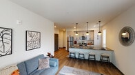 This single-floor residence at 6105 N Rural St in Indianapolis offers a thoughtfully designed open-concept layout that seamlessly connects the living, dining, and kitchen areas. Warm hardwood-style flooring runs throughout the main living spaces, complementing the clean, contemporary aesthetic defined by white walls and modern finishes.

The kitchen is a standout feature, equipped with stainless steel appliances including a refrigerator, range, and over-the-range microwave. Crisp white shaker-style cabinetry with matte black hardware reaches to the ceiling, maximizing storage. A large island with dark quartz countertops provides seating for multiple bar stools and is illuminated by a trio of stylish globe pendant lights. Multiple windows allow natural light to fill the space.

The living area is bright and comfortable, with natural light streaming through well-placed windows and ample wall space for décor.

Both bedrooms feature plush carpeting, natural light from windows, and organized closets with built-in shelving. A sliding barn door adds a modern touch to the primary bedroom's layout.

The two bathrooms are finished with white shaker vanities, dark quartz countertops, undermount sinks, and matte black hardware. One bathroom features a tub-shower combination, while both include large mirrors and practical storage.