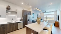 Located at 3811 Commerce Way in Sacramento, CA, this well-appointed one-bedroom, one-bathroom residence offers a thoughtfully designed open-concept floor plan. Light wood flooring flows throughout the main living areas, complementing the neutral palette and modern finishes found across the space.

The combined kitchen and living room serves as the heart of the home. The kitchen features two-tone cabinetry — upper white cabinets paired with rich wood-tone lower cabinets — accented by a textured white backsplash, quartz countertops, stainless steel appliances, and a central island with bar seating. The adjacent living area is bright and airy, with large windows offering sweeping outdoor views, a ceiling fan overhead, and a transom window near the entry door that draws in additional natural light.

The bedroom is a comfortable retreat with plush carpeting, a large window with balcony views, recessed lighting, and a stylish sliding barn door that connects to a dedicated closet. The bathroom is clean and functional, featuring a full tub-shower combination with matte black fixtures and light wood-tone flooring. Throughout the residence, crisp white walls, black hardware accents, and contemporary design choices create a cohesive, modern aesthetic.