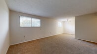 Located at 2342 Crimson Ln in Crescent Springs, Kentucky, this single-floor residence offers a practical and straightforward layout across two bedrooms, one bathroom, a kitchen, and a connecting hallway. The living area is generously sized, featuring neutral-toned carpet flooring, textured ceilings, and multiple windows fitted with blinds that allow natural light to fill the space. A ceiling fan is also present, adding to the room's functionality. The primary bedroom is notably spacious, carpeted, and includes a window that brings in natural light, with direct access to the hallway. The second bedroom, also carpeted, offers a quieter, more compact space with a closet. The kitchen is equipped with wood-toned cabinetry, dark speckled countertops, and a range, offering a compact yet functional cooking environment. The bathroom is clean and utilitarian, featuring a full-size soaking tub with an overhead shower and standard fixtures. Wall-mounted heating vents are present throughout the unit, and neutral wall tones throughout contribute to a simple, cohesive aesthetic. The layout, as visible in the dollhouse view, is efficiently organized with rooms flowing logically from the central hallway.