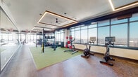 Located at 131 Mamaroneck Ave in White Plains, NY, this expansive fitness center is a thoughtfully designed facility offering a comprehensive workout experience across multiple training zones. Floor-to-ceiling windows line the perimeter, flooding the space with natural light and providing sweeping elevated views of the White Plains cityscape. The layout is divided into distinct functional areas, each tailored to a specific style of training. A dedicated cardio zone features a row of treadmills, stationary bikes, and rowing machines equipped with interactive screens, all positioned to maximize the panoramic views. An adjacent functional training area is anchored by a large overhead rig system fitted with TRX suspension straps, alongside a turf zone stocked with kettlebells, medicine balls, and plyo boxes for dynamic movement work. The strength training section is equipped with a cable machine, a dumbbell rack, and a weight bench, complemented by full-length mirrors and exposed ductwork that lend an industrial character to the space. Recessed tray ceilings with warm linear lighting and ceiling fans add architectural depth and comfort throughout. A separate glass-enclosed studio offers a quieter space for stretching, yoga, or small group sessions with stability balls. The combination of elevated design, abundant natural light, and diverse equipment makes this a highly functional and visually impressive fitness facility.