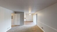This single-floor residence offers a straightforward, functional layout with a neutral color palette and a variety of practical finishes throughout. The living area is carpeted and features a distinctive white vertical shiplap accent wall, adding a touch of architectural character to the space. A textured ceiling and soft gray wall tones create a calm, understated ambiance. The open sightline from the living area into the adjacent room—equipped with a ceiling fan and sliding glass door that invites natural light—provides a sense of connected, flowing space.

The kitchen is outfitted with white cabinetry, brown laminate countertops, a white double-basin sink, and a coil-burner electric range, offering a clean and efficient cooking space. An overhead exhaust hood and upper cabinets with decorative trim provide additional storage and character.

The bedrooms are carpeted and well-proportioned, each featuring the same vertical shiplap accent wall detailing. One bedroom includes a built-in closet with bifold doors, offering practical storage. Windows in the bedrooms allow natural light to filter in from outside.

The bathroom includes a full tub-shower combination with a built-in shelving unit, chrome fixtures, and bright overhead lighting, maintaining the clean and functional tone found throughout the rest of the home.