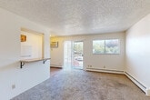 Located at 1709 31st Street Rd in Greeley, Colorado, this efficiently designed single-floor unit makes smart use of its compact footprint. The combined kitchen and living area forms the heart of the space, with the two zones separated by a practical breakfast bar counter with bracket supports — ideal for casual dining or additional workspace. The kitchen is outfitted with warm-toned natural wood cabinetry, a full-size white refrigerator, an electric range with overhead ventilation, and light wood-look vinyl flooring that adds warmth and durability. The living area transitions to plush carpeting and features a textured ceiling, a baseboard heating unit, and a wall-mounted air conditioning unit for year-round comfort. A sliding glass door floods the living room with natural light and opens to an outdoor balcony with views of surrounding greenery. An additional window further enhances the bright, airy feel of the room. The hallway connecting the rooms features the same light wood-look flooring and includes a spacious closet with sliding doors. The bathroom and an additional closet complete the layout, offering practical storage solutions. Overall, the unit presents a clean, neutral palette with a functional and straightforward design, well-suited for efficient everyday living.