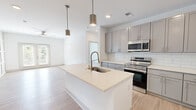 This single-floor residence in Carmel, Indiana offers a well-appointed layout accommodating two bedrooms and two bathrooms within a efficiently utilized footprint. The open-concept kitchen serves as a central highlight, featuring gray shaker-style cabinetry, white subway tile backsplash, light quartz countertops, and a central island with an undermount sink and modern pull-down faucet. Stainless steel appliances, including an electric range and built-in microwave, complete the kitchen. Cylindrical pendant lights add a contemporary touch overhead. Light-toned hardwood-style flooring runs throughout the main living areas, connecting the kitchen seamlessly to the living room, which features a decorative board-and-batten accent wall, ceiling fan, and French doors providing natural light and outdoor views. The bedrooms are carpeted and bright, with windows overlooking greenery. The primary bedroom includes access to a spacious walk-in closet with wire shelving systems. The primary bathroom features a dual-sink vanity with gray cabinetry, quartz countertops, pendant lighting, a framed mirror, and a tub-shower combination with large-format white subway tile surround.