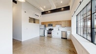 Located at 21 Erie Blvd in Albany, NY, this one-bedroom, one-bathroom unit showcases a compelling industrial aesthetic with modern finishes throughout. Polished concrete floors run seamlessly across the entire space, complemented by soaring ceilings with exposed structural steel beams and a coffered ceiling detail in the kitchen-living area that adds architectural character.

The open-concept kitchen and living room form the heart of the unit, featuring a well-appointed kitchen with a mix of warm wood upper cabinetry and crisp white lower cabinets, stainless steel appliances including a refrigerator, range, microwave, and dishwasher, and ample counter space. Large industrial-style windows invite generous natural light and offer views of the surrounding area.

The bedroom is a well-proportioned retreat with polished concrete floors, high ceilings, an exposed steel column, and two closets providing practical storage. Dark-framed doors throughout the unit reinforce the industrial design language.

The bathroom is finished with large hexagonal gray floor tiles, a white vanity with modern black hardware, and clean white walls, striking a balance between contemporary style and functionality. A dedicated laundry area and a hallway with louvered closet doors add convenience. A wall-mounted mini-split system provides climate control throughout this thoughtfully designed urban residence.