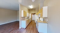 Located at 1830 Wiltsey Rd S in Salem, Oregon, this one-bedroom, one-bathroom unit offers a well-organized single-floor layout that makes efficient use of its space. The galley-style kitchen is a functional highlight, featuring light wood cabinetry extending to the ceiling for ample storage, laminate countertops, a double sink, a dishwasher, and a white electric range and refrigerator. The kitchen opens toward the living area, which is bathed in natural light from a sliding glass door that leads to a private balcony overlooking lush greenery — a serene outdoor connection. Warm, dark hardwood-style flooring runs throughout the main living areas, lending a cohesive and inviting feel. The bedroom is generously sized, finished with plush carpet for comfort, and features a large window framing views of surrounding trees. A walk-in closet provides notable storage capacity. The bathroom is well-appointed with light wood cabinetry, a wide vanity with a single sink, and neutral tile flooring that complements the overall warm, earthy color palette found throughout the unit. Warm beige tones on the walls, ceiling fans, and consistent finishes give the entire space a clean, comfortable, and cohesive ambiance.