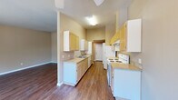 Located at 1830 Wiltsey Rd S in Salem, Oregon, this one-bedroom, one-bathroom unit offers a well-organized single-floor layout that makes efficient use of its space. The galley-style kitchen is a functional highlight, featuring light wood cabinetry extending to the ceiling for ample storage, laminate countertops, a double sink, a dishwasher, and a white electric range and refrigerator. The kitchen opens toward the living area, which is bathed in natural light from a sliding glass door that leads to a private balcony overlooking lush greenery — a serene outdoor connection. Warm, dark hardwood-style flooring runs throughout the main living areas, lending a cohesive and inviting feel. The bedroom is generously sized, finished with plush carpet for comfort, and features a large window framing views of surrounding trees. A walk-in closet provides notable storage capacity. The bathroom is well-appointed with light wood cabinetry, a wide vanity with a single sink, and neutral tile flooring that complements the overall warm, earthy color palette found throughout the unit. Warm beige tones on the walls, ceiling fans, and consistent finishes give the entire space a clean, comfortable, and cohesive ambiance.