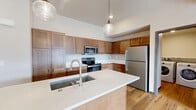 Located in Appleton, Wisconsin, this two-story, 2-bedroom, 2-bathroom home offers a well-designed layout across two levels. The main living floor hosts an open-concept kitchen and living room, where warm hardwood flooring flows throughout. The kitchen is outfitted with rich wood cabinetry, stainless steel appliances including a range, over-the-range microwave, and refrigerator, complemented by crisp white countertops and a large center island with a double undermount sink and pendant lighting above. The adjoining living room features recessed lighting, baseboard heating, and a sliding glass door that opens to a private balcony, bringing in natural light and outdoor views. Upstairs, two carpeted bedrooms provide comfortable retreats, each with ceiling fans and windows allowing natural light. The generously sized primary bedroom includes access to a well-appointed bathroom featuring dark wood cabinetry, tile flooring, a walk-in shower, and a walk-in closet with built-in shelving and hanging rods. A second full bathroom and a dedicated in-unit laundry room with a full-size washer and dryer round out the upper level. A carpeted staircase with a metal handrail connects the entrance level to the main living space, completing this functional and modern home.