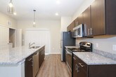 This two-floor residence combines modern finishes with a functional, open layout. The main living area flows seamlessly into a well-designed kitchen, where dark espresso cabinetry contrasts beautifully with granite countertops and stainless steel appliances, including a refrigerator, range, and microwave. A central island with a built-in sink provides additional workspace and serves as a natural gathering point, illuminated by stylish pendant lighting overhead. Light wood-look flooring extends throughout the main level, complemented by recessed lighting and a ceiling fan that enhance the bright, airy atmosphere. A half bath on the main floor adds everyday convenience. Upstairs, the bedrooms are generously proportioned, each fitted with ceiling fans and plush carpeting for comfort. Multiple windows dressed with blinds allow natural light to filter in, creating a warm and welcoming feel. The bathrooms are consistently appointed with dark wood vanities, granite countertops, and shower-tub combinations with light wood-look flooring. The primary bedroom suite benefits from direct access to its own private bathroom. Throughout the space, neutral wall tones and clean white trim provide a cohesive, move-in-ready aesthetic.