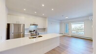 Located at 517 67 Ave SW in Calgary, Alberta, this fourth-floor one-bedroom unit offers a well-designed open-concept layout with clean, modern finishes throughout. Light hardwood flooring flows seamlessly across the entire space, complementing the bright white walls and recessed pot lighting that create a fresh, airy atmosphere.

The kitchen serves as the centerpiece of the main living area, featuring a large white waterfall-edge island with an undermount sink, crisp white cabinetry, subway tile backsplash, and stainless steel appliances including a refrigerator and electric range. The open layout allows the kitchen to connect effortlessly to the living area, which is bathed in natural light from a large window and a glass-paneled door leading to a private balcony with outdoor views.

The bedroom is generously proportioned, offering a large picture window with sweeping views of the Calgary skyline and surrounding neighbourhood. A dedicated full bathroom with a bathtub/shower combination is conveniently accessible from within the unit. A stacked washer and dryer unit is also included in-suite, adding everyday practicality. A wall-mounted mini-split system provides efficient climate control throughout the space. This unit offers a compact yet functional and stylish urban living experience.