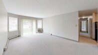 Located at 420 Riverglade Dr in Amherst, MA, this single-floor residence offers three bedrooms, two full bathrooms, and a well-organized layout designed for comfortable living. The open-concept kitchen and living area form the heart of the home, with the kitchen featuring rich dark wood cabinetry, light countertops, a full suite of black appliances including a refrigerator, range, and dishwasher, and light wood-style flooring. A pass-through counter connects the kitchen to the adjoining living space, enhancing the open feel. The spacious living room is carpeted and bathed in natural light, with a sliding glass door and flanking windows offering direct outdoor views and access. The bedrooms are carpeted and neutrally finished, with the primary bedroom offering generous dimensions and a walk-in closet equipped with wire shelving. Both bathrooms are finished with wood-style flooring, dark wood vanities, and mirrors. One bathroom includes a full soaking tub and shower combination. Baseboard heating and wall-unit air conditioning are present throughout, ensuring year-round comfort. The neutral gray and white color palette creates a clean, cohesive aesthetic throughout the entire residence.