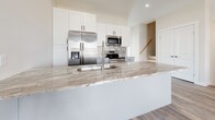 Located in East Lyme, Connecticut, this modern multi-floor residence offers four bedrooms and three bathrooms thoughtfully distributed across three levels. The entry level welcomes you with durable hardwood-style flooring, neutral warm tones, and natural light from well-placed windows, creating a bright and open atmosphere. A wall-mounted mini-split system provides efficient climate control throughout.

The kitchen is a true highlight, featuring crisp white shaker cabinetry, a large center island topped with striking granite countertops, a deep undermount sink with a contemporary faucet, and a full suite of stainless steel appliances including a French door refrigerator, range, and over-the-range microwave. A mosaic tile backsplash adds a refined touch to the cooking area.

The bedrooms are generously sized with hardwood-style flooring and ceiling fans in select rooms, offering comfort and versatility. The primary bedroom connects to a spacious walk-in closet with wire shelving, maximizing storage. Bathrooms are finished with elegant marble-look tile flooring, vanities with ample storage, and clean white fixtures — one bathroom features a tiled walk-in shower, while another offers a full tub-shower combination. The overall aesthetic is clean, contemporary, and move-in ready.