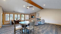 Located at Decatur Plaza in Omaha, Nebraska, this single-floor community clubhouse offers a thoughtfully designed layout that blends comfort and functionality. The open-concept living room impresses with soaring vaulted ceilings accented by exposed wood beams, plush carpeting, and a tile-surround fireplace with a built-in entertainment niche — creating a warm, welcoming gathering space. Large windows allow natural light to fill the room, enhancing the relaxed ambiance.

The adjacent dining area features tile flooring, a chandelier overhead, and ample space for group seating around a central round table. Tasteful wall art and neutral tones give the room a clean, modern feel. The kitchen is well-equipped with warm oak cabinetry, tile backsplash, stainless steel appliances including a full-size refrigerator, and a breakfast bar with stylish swivel bar stools — ideal for casual dining or socializing.

The dedicated exercise room provides a practical fitness space outfitted with cardio equipment, a full rack of dumbbells, a wall-mounted television, and access to restroom facilities. A door connects directly to the outdoor pool area, which features lounge seating and a resort-style pool, extending the recreational amenities of this versatile community space.