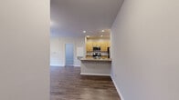 This single-story residence is thoughtfully designed with a functional, open layout. The kitchen serves as a central feature, equipped with stainless steel appliances including a gas range, microwave, and refrigerator, complemented by light wood cabinetry and granite-style countertops. A peninsula with an integrated sink extends into the living area, creating a natural divide between cooking and living spaces while maintaining an open feel. Recessed lighting illuminates the kitchen throughout.

The living area is spacious and bright, featuring hardwood-style flooring and a sliding glass door that opens onto a private balcony overlooking a natural wooded landscape. The bedroom offers plush carpeting, ample wall space, and direct access to a closet with built-in shelving, as well as a connecting bathroom. The bathroom includes a tiled shower-tub combination and hardwood-style flooring.

A dedicated laundry area houses a full-size washer and dryer alongside additional wire shelving for storage. Neutral wall tones and clean white trim are consistent throughout, contributing to a cohesive and move-in-ready aesthetic.