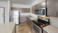 This single-floor, 2-bedroom, 2-bathroom residence offers a well-designed layout with a blend of modern finishes and functional living spaces. The kitchen serves as a highlight of the home, featuring rich dark-stained cabinetry, light granite-style countertops, and a full suite of stainless steel appliances including a refrigerator, electric range, over-the-range microwave, and dishwasher. Wood-look plank flooring runs throughout the main living areas and bathrooms, lending a warm, cohesive aesthetic. A kitchen island provides additional counter space and casual dining potential. The bedrooms are carpeted for comfort and each includes a window with blinds, allowing for natural light. Baseboard heating ensures efficient climate control in each room. The primary bathroom connects to a walk-in closet and features dark cabinetry with granite-style counters, while the secondary bathroom offers a full soaking tub and shower combo with clean white surroundings and wood-look flooring. A dedicated in-unit laundry area houses a full-size side-by-side washer and dryer, adding everyday convenience. Neutral wall tones throughout create a calm, move-in ready atmosphere suitable for a variety of living arrangements.