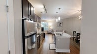 Located at 130 Sharon Township Lane in Charlotte, NC, this one-bedroom, one-bathroom unit offers a thoughtfully designed layout that makes efficient use of its compact footprint. The open-concept kitchen and living area serves as the heart of the space, featuring rich dark espresso cabinetry, stainless steel appliances, a subway tile backsplash, and a curved granite-topped island with a built-in sink. Pendant lighting and a track light system illuminate the kitchen, while wood-look flooring extends throughout, adding warmth and continuity.

The living area is bright and inviting, with a large window that draws in natural light and provides views of the surrounding greenery. Neutral gray walls and clean architectural lines give the space a calm, modern aesthetic.

The bedroom is comfortably sized, featuring plush carpet, a ceiling fan, and soft neutral tones. It includes a dedicated closet for storage. The bathroom is well-finished, offering a dark vanity with a granite countertop, a tub-shower combination, and wood-look flooring that mirrors the rest of the unit.

Overall, the space presents a cohesive, modern design with quality finishes throughout, suited for comfortable single-occupant living in a desirable Charlotte neighborhood.
