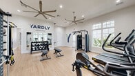 The Yardly Crossings fitness center at 3800 Viceroy Place in DeLand, Florida is a thoughtfully designed exercise facility offering a comprehensive workout experience within a bright, modern space. The room features light hardwood-style flooring and crisp white walls, creating a clean and energizing atmosphere. Large windows on multiple walls flood the space with natural light while providing views of the surrounding greenery, and overhead ceiling fans ensure comfortable air circulation throughout.

The facility is well-appointed with a diverse selection of equipment to support a full-body fitness routine. Cardio offerings include treadmills, an elliptical trainer, a rowing machine, and stationary bikes. A multi-station cable machine and a power rack with an integrated cable system support strength and functional training, while a dedicated free weights area features a full dumbbell rack, medicine balls, stability balls, and adjustable benches. Floor-mounted mirrors enhance the sense of space and allow users to monitor their form during workouts. A wall-mounted flat-screen television adds an entertainment option for extended training sessions. The space is branded prominently with the Yardly Crossings logo, reinforcing its identity as a community amenity designed to support an active lifestyle for residents.