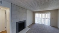 This single-floor, one-bedroom, one-bathroom unit offers a well-organized layout designed for efficient, comfortable living. The living area serves as the focal point of the space, highlighted by a striking floor-to-ceiling tile-clad fireplace wall in a cool grey tone, providing both a visual anchor and a functional heating feature. The fireplace surround is finished with dark tile, adding a clean contrast to the lighter wall tiles. Carpeting covers the main living area, contributing a warm, understated texture underfoot, while tile flooring near the fireplace hearth provides a practical transition zone. A large sliding glass door fitted with vertical blinds allows generous natural light to filter into the room, brightening the space and offering potential outdoor access or views. The textured ceiling adds a classic finish consistent throughout the unit. The overall ambiance is neutral and clean, with a straightforward aesthetic that provides a versatile backdrop for personalization. The single-floor layout ensures easy navigation throughout, making this unit a practical and inviting living space.