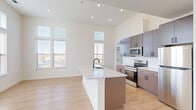 Located at 103 East 2nd Street in Richmond, VA, this well-appointed 2-bedroom, 2-bathroom residence offers a thoughtfully designed open-concept floor plan. The combined kitchen and living area is immediately impressive, showcasing soaring ceilings and tall windows that flood the space with natural light and frame views of the surrounding cityscape. Light-toned hardwood-style flooring extends throughout the main living areas, enhancing the bright and airy ambiance. The contemporary kitchen is a standout feature, centered around a large island with a crisp white countertop and an undermount sink with a matte black faucet. Rich dark cabinetry lines the walls alongside white subway tile backsplash, and the kitchen is fully equipped with stainless steel appliances including a range, microwave, and refrigerator. Both bedrooms are generously proportioned, featuring plush carpeting, ceiling fans with lighting, and windows overlooking the city. The primary bedroom offers comfortable scale and connects conveniently to its own bathroom. The bathrooms are cleanly finished with wood-toned vanities, white quartz countertops, matte black hardware, and tiled tub-shower combinations. A dedicated closet completes this polished, move-in-ready Richmond residence.