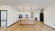 Located at 32449 North Gary Road in San Tan Valley, AZ, this single-story home offers three bedrooms, two bathrooms, and a thoughtfully designed open-concept layout. The kitchen and living area form the heart of the home, anchored by a substantial wood-wrapped island with a quartz countertop and an undermount sink with a matte black gooseneck faucet. Two geometric cage pendant lights hang above the island, complementing recessed lighting throughout. Cabinetry blends white upper cabinets with warm wood-toned lower cabinets, and stainless steel appliances — including a French door refrigerator, built-in microwave, and range — complete the culinary space. Light wood-look flooring flows seamlessly throughout the home, enhancing the bright, clean aesthetic created by crisp white walls. The living area features a ceiling fan and access to the exterior through a black-framed door, with a window allowing natural light to fill the room. Stylish gray panel doors add a sophisticated accent. The primary bedroom includes a well-organized walk-in closet with built-in shelving, hanging rods, and a four-drawer dresser unit. The bathrooms are finished with white vanities, quartz counters, wood-look flooring, and a glass-enclosed walk-in shower with white subway tile and matte black fixtures.