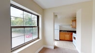 This single-floor unit offers a thoughtful layout that combines classic architectural character with practical living spaces. The open living area is generously sized, featuring neutral-toned carpet, recessed lighting, and multiple windows that invite abundant natural light and views of surrounding greenery. The space flows seamlessly from the main living area toward the kitchen and private rooms.

The kitchen is efficiently designed, equipped with warm oak cabinetry, dark granite-style countertops, a double stainless steel sink, a gas range, refrigerator, and an over-the-range microwave. Light tile flooring and open shelving add to the kitchen's functional appeal.

A standout feature of this unit is the exposed brick wall found in one of the bedrooms, lending the space a distinctive, loft-inspired character. This room is brightened by a large window framing outdoor views and is finished with plush carpeting. Additional bedrooms are finished with the same neutral carpet and warm paint tones, providing a clean and versatile backdrop.

The bathroom continues the brick accent theme, with a window for natural light, tile flooring, and a full tub and shower combination. Throughout the unit, cream-toned walls, white trim, and consistent finishes create a cohesive and inviting atmosphere well-suited for comfortable everyday living.