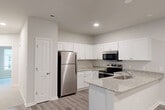 Located at 2308 Holiday Loop in Reidsville, NC, this 2-bedroom, 3-bathroom single-floor home offers a well-designed layout with a clean, modern aesthetic throughout. The open-concept living, dining, and kitchen area serves as the heart of the home, finished with durable wood-look plank flooring. The kitchen is outfitted with crisp white shaker-style cabinetry, granite countertops, a peninsula with an integrated sink, and a full suite of stainless steel appliances including a refrigerator, range, and microwave. The living area features soft carpeting and a set of glass French doors that open to a private balcony, allowing natural light to fill the space. The spacious primary bedroom includes a ceiling fan, plush carpet, and direct access to an en-suite bathroom featuring granite-topped vanity with white cabinetry. Two additional bathrooms serve the home, each finished with consistent granite and white cabinetry details. The second bedroom is generously sized with carpeted flooring and easy hallway access. Three closets provide ample storage throughout, and a dedicated laundry area adds everyday convenience. Neutral tones and consistent finishes create a cohesive, move-in-ready environment.