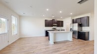 Located at 2920 Florence Dr in Gainesville, GA, this two-story home offers a thoughtfully designed layout across two well-proportioned floors. The main level features an open-concept kitchen and living room filled with natural light from multiple windows. The kitchen is a standout space, showcasing dark espresso cabinetry, granite countertops, a central island with a sink, and a full suite of stainless steel appliances, including a French door refrigerator, range, and microwave. Light hardwood-style flooring flows seamlessly throughout both levels, complementing the home's clean, modern aesthetic. A ceiling fan in the living area adds comfort and a welcoming touch. A pantry and dedicated laundry room with overhead wire shelving, washer and dryer hookups, and a utility drain round out the main floor's functional spaces. Upstairs, the primary bedroom impresses with a tray ceiling, ceiling fan, dual windows, and a spacious walk-in closet with wire shelving. The primary bathroom features a glass-enclosed walk-in shower. Two additional bedrooms, each with light flooring and closet storage, provide versatile space. Three full bathrooms, a hallway, and a staircase complete this well-organized home, making it an excellent option for comfortable everyday living.