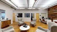 Located at 1278 W. Ninth Street in Cleveland's vibrant near-west side, this single-floor commercial space offers a compelling mix of industrial heritage and contemporary design. The open reception and lounge area sets an inviting tone, featuring warm hardwood flooring, exposed structural columns, and an open ceiling with visible ductwork that nods to the building's industrial roots. Comfortable lounge seating arranged around a central coffee table creates a welcoming gathering point, while interior windows with views into adjacent offices maintain visual connectivity throughout the space. A dedicated meeting area offers a round table with modern chairs, area rug, and bold orange accent seating nearby, lending color and energy to the layout. The space transitions into a spacious amenity and recreation zone featuring plush carpet, a full-size billiard table, and a cozy lounge anchored by a wood-paneled fireplace surrounded by vibrant orange armchairs and curated wall art. A game room with an exposed brick accent wall, foosball table, and mounted flat-screen TV adds a lively, social atmosphere. Throughout, recessed lighting, tasteful artwork, and a neutral gray-and-orange palette create a cohesive, professional yet approachable ambiance ideal for collaboration and community.