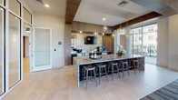 The Ledgewood Club Room at 1950 Route 46 in Netcong, NJ is a thoughtfully designed community amenity space that blends upscale aesthetics with a wide range of social and recreational functions across a single expansive floor. The lounge area serves as the centerpiece of the space, featuring a sleek floor-to-ceiling tile-clad fireplace wall with a wall-mounted television, complemented by contemporary furnishings including plush sectional seating, tufted ottomans, and a striking gold chain chandelier that adds a dramatic focal point overhead. Adjacent to the lounge, a well-appointed bar and kitchen area showcases a large granite-topped island with bar seating, pendant lighting, wood-paneled cabinetry, stainless steel appliances, and a dedicated coffee and beverage station. A separate seating area accommodates casual gatherings with clustered armchairs beneath a starburst chandelier. The game room wing features a pool table and shuffleboard table, both set on richly patterned carpet tiles. Café-style high-top tables positioned beside floor-to-ceiling windows provide views of the surrounding landscape, while a private conference room overlooks the outdoor pool and courtyard, filled with natural light through large glass panels. The overall ambiance is modern, polished, and inviting throughout.