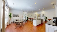 Located at 1 Madison Park Drive in Huntsville, Alabama, this single-floor community amenity space offers a well-rounded collection of shared facilities designed for comfort and convenience. The interior is finished with warm hardwood flooring throughout the main areas, crisp white walls, crown molding, and recessed lighting that creates a bright, welcoming atmosphere.

The open-concept social and kitchen area serves as the centerpiece of the space. A large island with dark granite countertops, a dual-basin sink, and leather bar stools anchors the kitchen, which features white cabinetry, subway tile backsplash, stainless steel appliances including a wall oven and microwave, and a built-in television. Adjacent to the kitchen is a casual lounge and dining area furnished with stylish geometric-patterned tables and wire-frame chairs. Large windows dressed with neutral drapes flood the space with natural light and offer views of lush greenery outside.

A foosball table adds a recreational touch to the lounge area. The space also includes a fully equipped fitness center visible in the floor plan, outfitted with a wide range of cardio and strength training equipment.

A dedicated pet grooming room features light tile flooring, a grooming station, built-in shelving stocked with pet care supplies, and a large window providing ample natural light — a thoughtful amenity for pet owners.