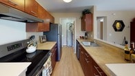 This upgraded Elm floor plan offers a thoughtfully designed single-level layout with two bedrooms and one full bathroom. The galley-style kitchen is a standout feature, showcasing rich cherry wood cabinetry, upgraded countertops, hardwood-style flooring, and stainless steel appliances including a refrigerator and dishwasher — providing both style and functionality. The living area is open and inviting, featuring carpet flooring and a half-wall divider that adds architectural definition to the space. A dedicated dining area benefits from large windows that invite natural light and offer pleasant outdoor views, complemented by a ceiling fan overhead. The primary bedroom is generously sized with soft carpet, a wide window, and a built-in closet with shelving for organized storage. The second bedroom is equally versatile, well-suited as a home office or guest room, complete with a large window and ample floor space. The full bathroom features tile flooring, a vanity with matching cabinetry, and a shower-tub combination. A dedicated entryway with coat hooks and tile flooring provides a practical transition space. Throughout the home, warm neutral tones and upgraded finishes create a cohesive and comfortable living environment.