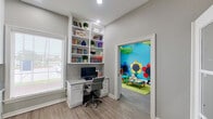 This well-designed single-floor space seamlessly blends productivity and play in a bright, welcoming environment. The main office area features a built-in white shelving unit with a granite-topped desk, offering ample storage for books and decorative items. Light hardwood-style flooring, neutral gray walls, and large windows fitted with horizontal blinds allow natural light to fill the room. A set of elegant French doors with glass panels adds architectural character and connects the space to an adjacent area.

Directly accessible from the office is a vibrant children's playroom that bursts with color and imagination. The room is painted in bold turquoise with large, hand-painted flower murals adorning the walls and decorative oversized leaf panels hanging from the ceiling, creating an immersive garden-inspired environment. Soft animal-shaped seating and a child-sized play table complete the space.

A hallway leads to a practical refreshment nook featuring white cabinetry, a marble-style countertop with subway tile backsplash, and dual water fountains mounted conveniently in the corridor. A restroom is also accessible nearby, rounding out the functional amenities. Recessed lighting throughout ensures a consistently well-lit and inviting atmosphere across all areas.