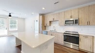 This single-floor residence showcases a cohesive modern design throughout, blending light wood tones, white quartz surfaces, and warm hardwood-style flooring for a clean, contemporary aesthetic. The kitchen is a standout feature, equipped with light wood cabinetry accented by matte black hardware, a white subway tile backsplash, stainless steel appliances including a refrigerator with ice maker, range, microwave, and dishwasher, and a generous quartz island that provides ample prep and storage space. Recessed lighting illuminates the kitchen, which flows openly into the adjoining living area. The bedrooms are carpeted and well-proportioned, each featuring ceiling fans with light fixtures. Natural light enters through double windows fitted with blinds, creating a bright and airy atmosphere. One bedroom includes direct access to a spacious walk-in closet outfitted with wire shelving, as well as an en-suite bathroom. The bathrooms continue the design language of the kitchen, featuring light wood vanities, white quartz countertops, undermount sinks with chrome faucets, tiled walk-in showers, and large mirrors. The primary bathroom offers a dual-sink vanity, adding a practical and elegant touch. Throughout, white walls and clean lines contribute to a fresh, move-in-ready environment.