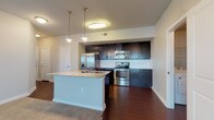 This single-story 2-bedroom, 2-bathroom residence offers a thoughtfully designed open-concept floor plan with a seamless blend of modern finishes and functional living spaces. The kitchen serves as a central highlight, featuring dark espresso cabinetry, granite countertops, a white subway tile backsplash, and a full suite of stainless steel appliances including a French door refrigerator, electric range, and over-the-range microwave. A peninsula island with a granite surface and undermount sink provides additional prep space and serves as a natural divider between the kitchen and the adjoining living area. Rich hardwood-style flooring runs throughout the kitchen and bathrooms, while soft carpet covers the living areas and bedrooms. The spacious bedrooms are filled with natural light from large windows fitted with horizontal blinds, and the primary bedroom includes a ceiling fan. Both bathrooms are finished with dark vanity cabinetry, granite countertops, and tub-shower combinations with white tile surrounds. A dedicated laundry area with in-unit washer and dryer connections adds convenience. The living area is generously proportioned with neutral tones and track lighting, creating a bright, versatile space throughout.
