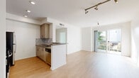 Located in Hollywood, Los Angeles, this single-floor residence offers four bedrooms and three bathrooms within a thoughtfully designed layout. The open-concept living and kitchen area serves as the heart of the home, featuring light hardwood flooring, track lighting, and a sliding glass door that opens to a private balcony with views of the surrounding neighborhood and lush palm trees. The kitchen is outfitted with stainless steel appliances, a gas range, dark granite-style countertops, warm wood cabinetry, and a decorative mosaic tile backsplash, alongside a peninsula that defines the space. The living area is bright and airy, bathed in natural light. The primary bedroom offers carpeted flooring, a sun-filled window with outdoor views, and access to a well-appointed bathroom featuring dual undermount sinks, wood cabinetry with brushed nickel hardware, and large-format tile flooring. Additional bathrooms include a full tub-shower combo with floor-to-ceiling tile surround. Bedrooms are generously sized with plush carpeting and ample natural light. Storage is well-addressed with dedicated closets featuring built-in shelving and hanging rods. Clean white walls and a neutral palette throughout lend the home a modern, move-in-ready ambiance.