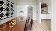 Located at 425 Williams Dr in Marietta, Georgia, this sophisticated single-floor residence blends classic architectural detail with refined modern sensibility. The entryway welcomes visitors with soaring ceilings, vertical shiplap paneling in crisp white, and wood-look tile flooring that flows throughout the space, creating a warm yet polished foundation. A striking glass-paneled front door bathes the entry in natural light while offering views to an outdoor terrace framed by a decorative wrought iron railing — a standout architectural feature that seamlessly connects the interior to the surrounding landscape of lush Georgia greenery.

The dining area is a well-appointed gathering space, anchored by a rich wood table surrounded by dark leather chairs. Vertical paneled walls in a soft neutral tone provide an elegant backdrop, complemented by a large-scale black-and-white houndstooth artwork that adds bold visual interest. Gold sphere decorative accents on the tabletop reflect light beautifully, lending a touch of glamour. Framed artwork adorns the adjacent wall, while floor-to-ceiling sliding glass doors open directly to the outdoor terrace, enhancing the sense of openness and bringing the outdoors in. A glimpse into a connected kitchen with cabinetry and tile backsplash suggests a thoughtfully designed and cohesive interior throughout.
