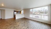 Located in Seattle's Beacon Hill area, Unit 204 at 4500 15th Ave S is a thoughtfully designed single-floor residence that balances modern finishes with functional living. Hardwood-style flooring flows consistently throughout the unit, providing a cohesive and contemporary feel.

The open living area is a standout feature, characterized by expansive corner windows that flood the space with natural light and offer views of the surrounding neighborhood. A sliding glass door in an adjoining room provides direct outdoor access and additional light. The layout, as seen in the floorplan, connects the living area seamlessly to the kitchen.

The kitchen is well-appointed with dark cabinetry, stone-look countertops, stainless steel appliances including a refrigerator, microwave, and range, and a double-basin sink beneath a window. Track lighting overhead enhances the functional workspace. A breakfast bar separates the kitchen from the living area.

The hallway leads to additional rooms, including a closet with built-in wire shelving for organized storage. Two bathrooms serve the unit: one features a vanity with dark cabinetry and a single sink, while the other includes a bathtub/shower combination. Neutral wall tones throughout maintain a clean, move-in-ready aesthetic.