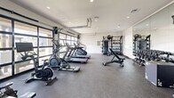 Located in Pflugerville, Texas, this fitness center is a well-equipped, single-floor exercise space designed to support a full range of workout routines. The room is finished with durable rubber flooring throughout, providing both safety and comfort during exercise. Recessed lighting illuminates the space evenly, complementing the clean white walls that give the interior a bright, modern aesthetic.

A defining architectural feature is the floor-to-ceiling glass garage doors that line one wall, flooding the space with natural light and offering views of the surrounding outdoor area. These doors also lend an open, airy feel to the room. A secondary set of glass-panel entry doors provides additional access.

The fitness center is outfitted with a comprehensive selection of equipment. Cardio machines include multiple treadmills, ellipticals, a stationary bike, a rowing machine, and a stair climber. For strength training, the space features a cable machine, an adjustable weight bench, and a full dumbbell rack. A large wall-mounted mirror on one side visually expands the room and aids in form correction during workouts. Equipment storage racks along the walls keep medicine balls and accessories neatly organized.

The overall ambiance is clean, functional, and purposefully designed, making this fitness center a capable and inviting space for residents to pursue their health and wellness goals.