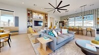 Located in Sun City, Arizona, this single-floor community space is a beautifully designed clubhouse that seamlessly blends a living room and dining area into one expansive, open-concept layout. The interior is defined by its contemporary aesthetic, featuring light-toned tile flooring, crisp white walls, and thoughtfully curated furnishings in a vibrant palette of teal, mustard yellow, and warm wood tones.

The living area is anchored by a generous sectional sofa, complemented by sculptural lounge chairs and a built-in entertainment wall with open shelving and a mounted flat-screen television. An oversized ceiling fan adds both function and visual interest overhead, while a bold geometric accent wallpaper brings personality to the space.

The dining area is equally impressive, with large floor-to-ceiling sliding glass doors that flood the room with natural light and offer direct views of the outdoor patio, where palm trees and shaded seating are visible. Marble-topped tables, pendant lighting with brass and copper accents, and built-in upholstered banquette seating with blue acoustic wall panels create a refined yet inviting atmosphere.

A kitchenette with counter seating and a patterned accent wall adds further functionality. The overall ambiance is modern, vibrant, and welcoming—ideal for community gatherings and social interaction.