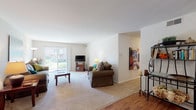 This thoughtfully designed single-floor residence offers a comfortable and functional layout across several well-defined living spaces. The expansive living room is a standout feature, finished with plush wall-to-wall carpeting and large sliding glass doors that invite abundant natural light while providing views of the outdoor greenery. The open feel of this space easily accommodates multiple seating arrangements and transitions smoothly into the rest of the home. Hardwood-style flooring extends through the dining area, which is highlighted by a ceiling fan with light fixture and direct sight lines into the kitchen. The kitchen is well-equipped, featuring rich cherry-toned cabinetry, dark granite-style countertops, stainless steel appliances including a gas range, over-the-range microwave, dishwasher, and refrigerator, all set atop matching hardwood-style flooring. The primary bedroom is generously sized with soft carpeting, access to a walk-in closet, and an en-suite bathroom. The bathroom includes a tiled tub-shower combination, vanity with storage, and tile flooring. A separate flex room with carpeting and a bright window serves well as a home office or secondary sitting area.