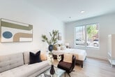 Located at 128 Maple St in Danvers, MA, this well-appointed studio delivers a smart, modern layout that maximizes every inch of its compact footprint. The open-plan living area is bright and airy, with crisp white walls, light hardwood-style flooring, and a large window that draws in generous natural light and views of the surrounding streetscape. The space comfortably accommodates both a living and sleeping area in a cohesive, functional arrangement.

The kitchen runs along one wall in a efficient galley configuration, showcasing slate-blue shaker cabinets, white quartz countertops with a marble-look tile backsplash, and stainless steel appliances including a range, dishwasher, and refrigerator. A breakfast bar with seating provides a casual dining option.

The bathroom is clean and contemporary, featuring a fully tiled walk-in shower with a frameless glass door and brushed gold fixtures. A dedicated laundry area includes a stacked full-size washer and dryer, adding notable convenience. Recessed lighting throughout and a cohesive neutral palette give the entire studio a polished, move-in-ready feel.