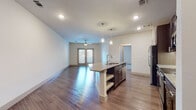 This single-floor residence offers a thoughtfully designed open-concept layout that seamlessly connects the kitchen, dining, and living areas. The kitchen is a standout feature, showcasing rich dark espresso cabinetry with sleek hardware, light granite countertops, a classic subway tile backsplash, and a full suite of stainless steel appliances including a refrigerator, electric range, and microwave. A central island with an integrated sink, open shelving below, and pendant lighting above serves as both a functional workspace and a natural gathering point. The expansive living area is finished with warm hardwood-style flooring that runs throughout the main living spaces, recessed lighting, and a ceiling fan. French-style doors provide natural light and lead to an outdoor area. The bedroom is carpeted for comfort, features a ceiling fan, and benefits from natural light through a slatted window. The bathroom is clean and well-appointed, with large-format tile surrounding the soaking tub and shower combo, complemented by chrome fixtures. A closet with double paneled doors adds practical storage. The overall ambiance is bright, contemporary, and move-in ready.